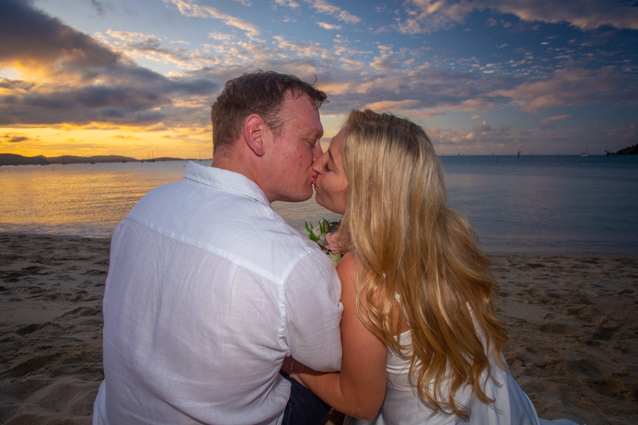 Bride and groom kissing on the beach at sunset