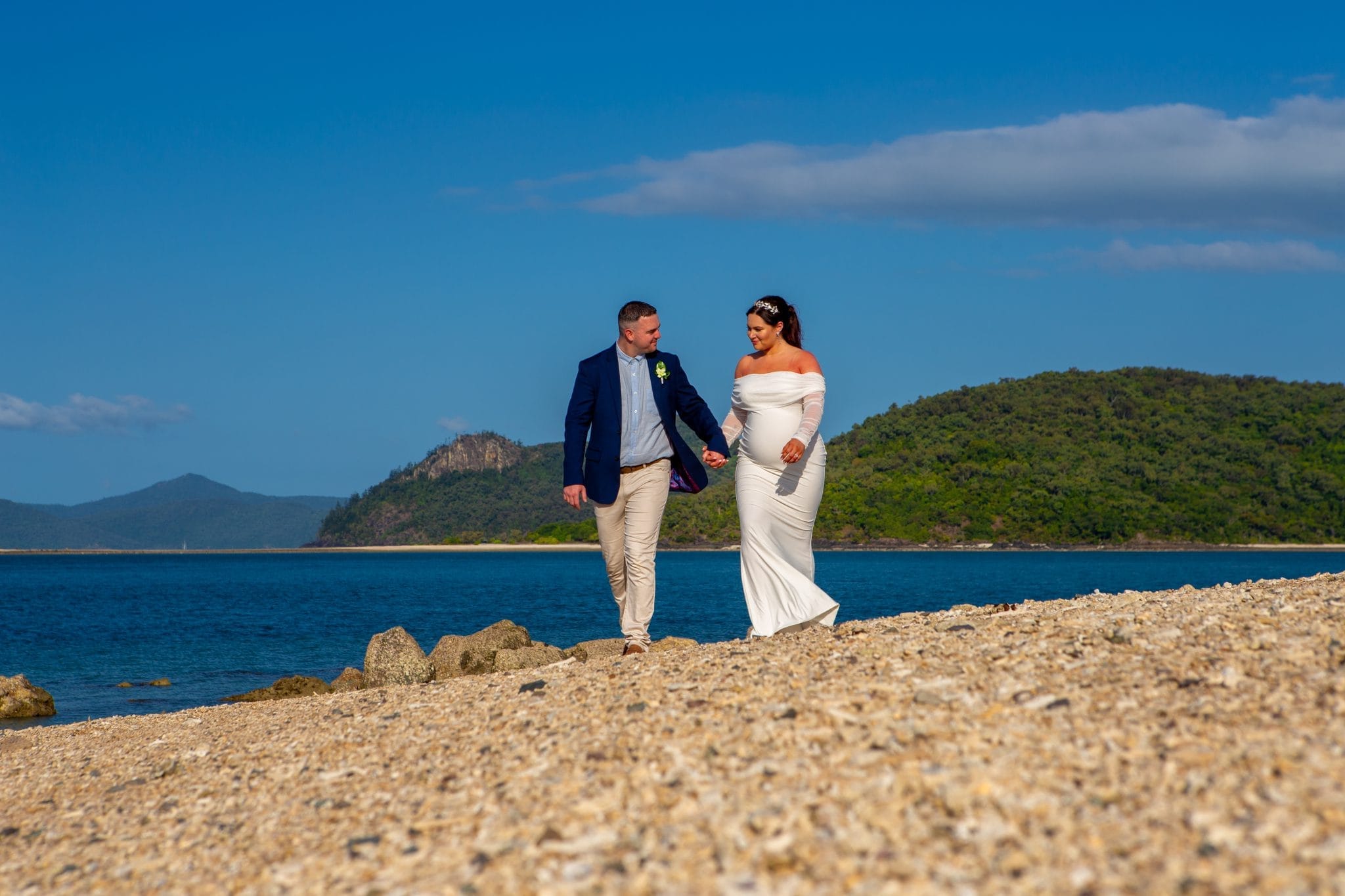 Bride and groom walking along a beach of coral and shells