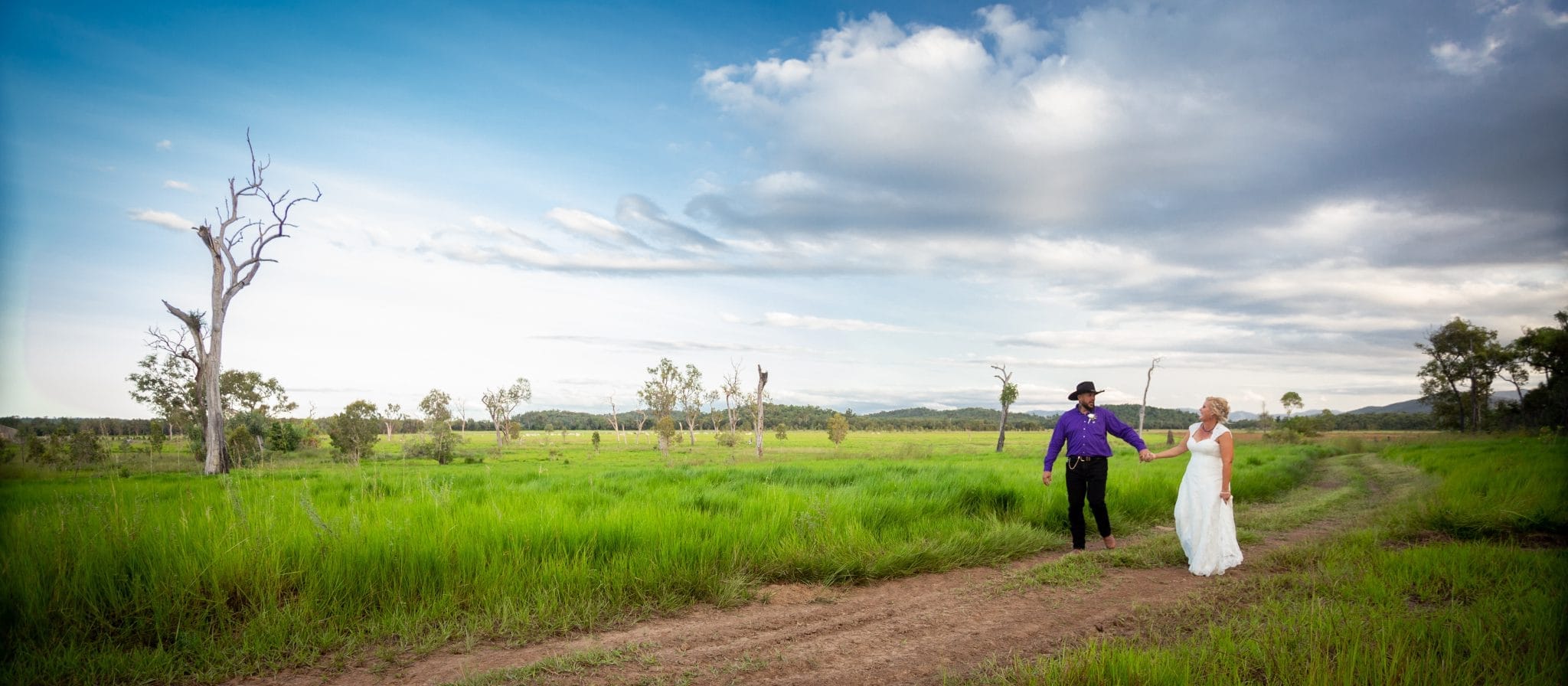 A man and a woman walking along a track. The man is wearing a purple shirt and black pants, the woman is wearing a wedding dress.