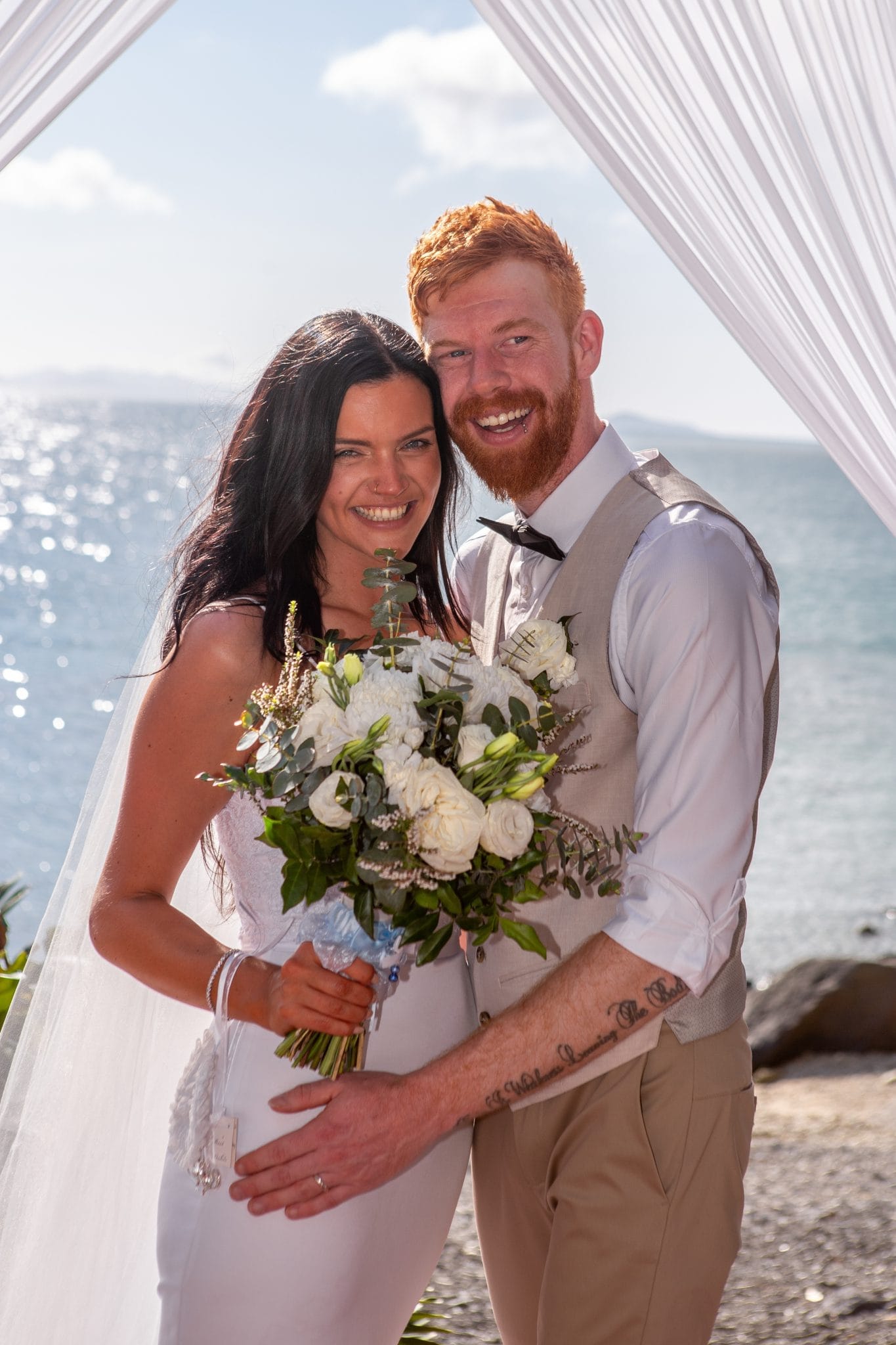 Bride and groom smiling together in front of the ocean