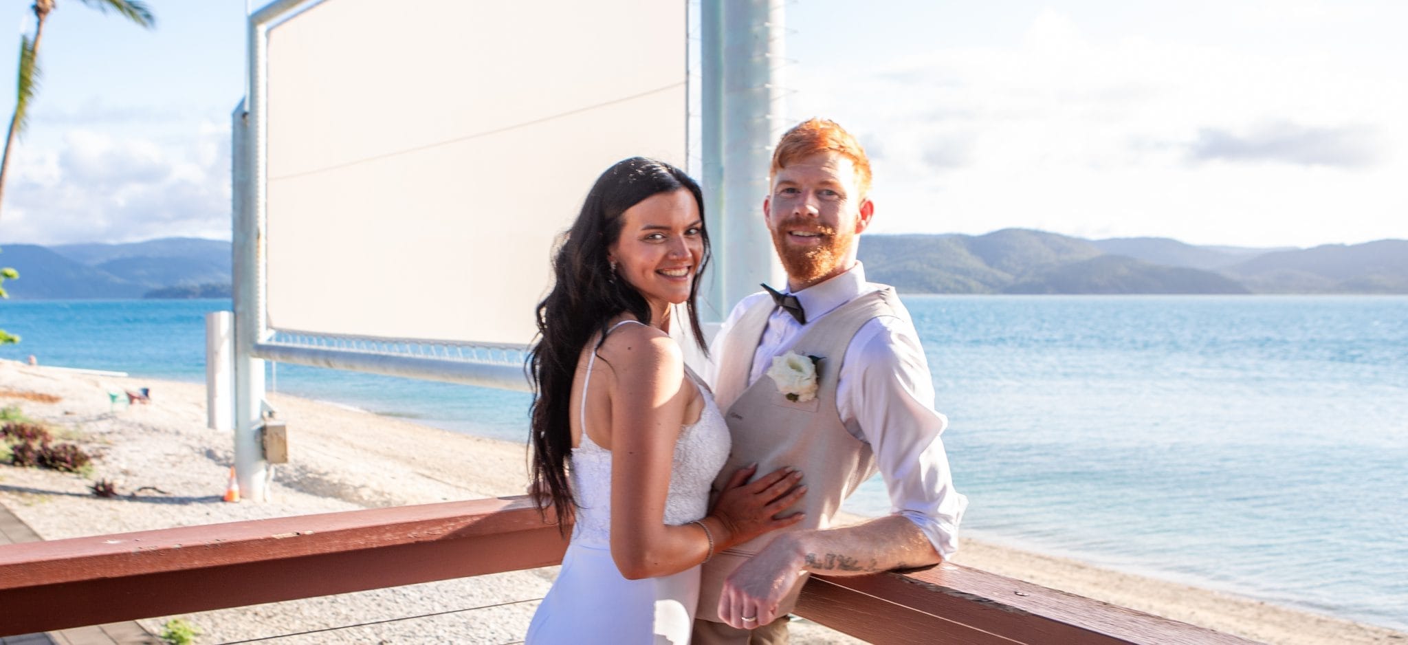 Bride and groom looking at the camera smiling together overlooking the ocean